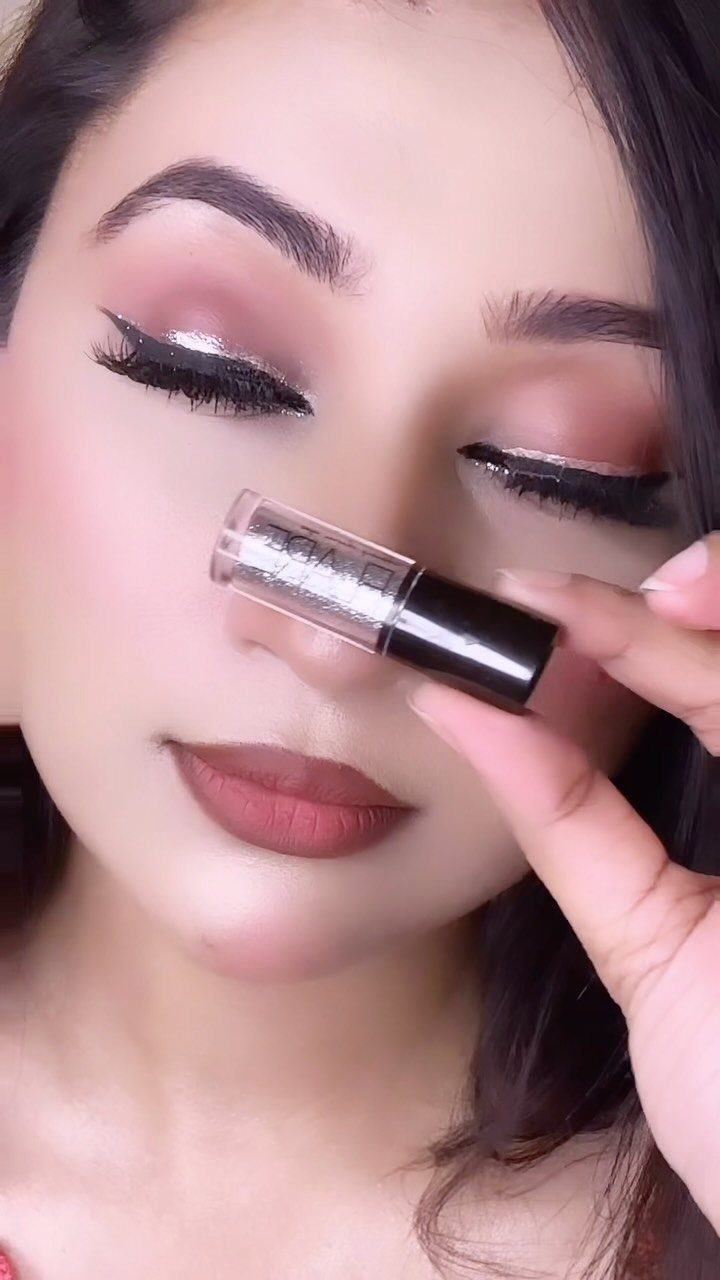 Woman with shimmering silver eyeshadow and matte brown lips holding a makeup bottle