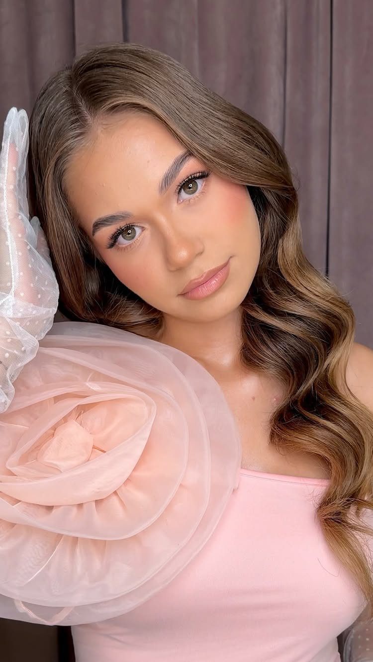 Young woman with green eyes wearing soft peach makeup and a pink dress.