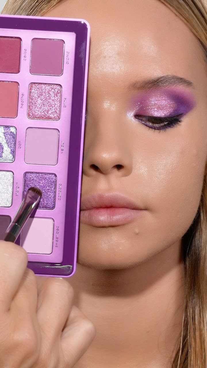 Woman with purple shimmer eyeshadow holding a purple eyeshadow palette next to her face