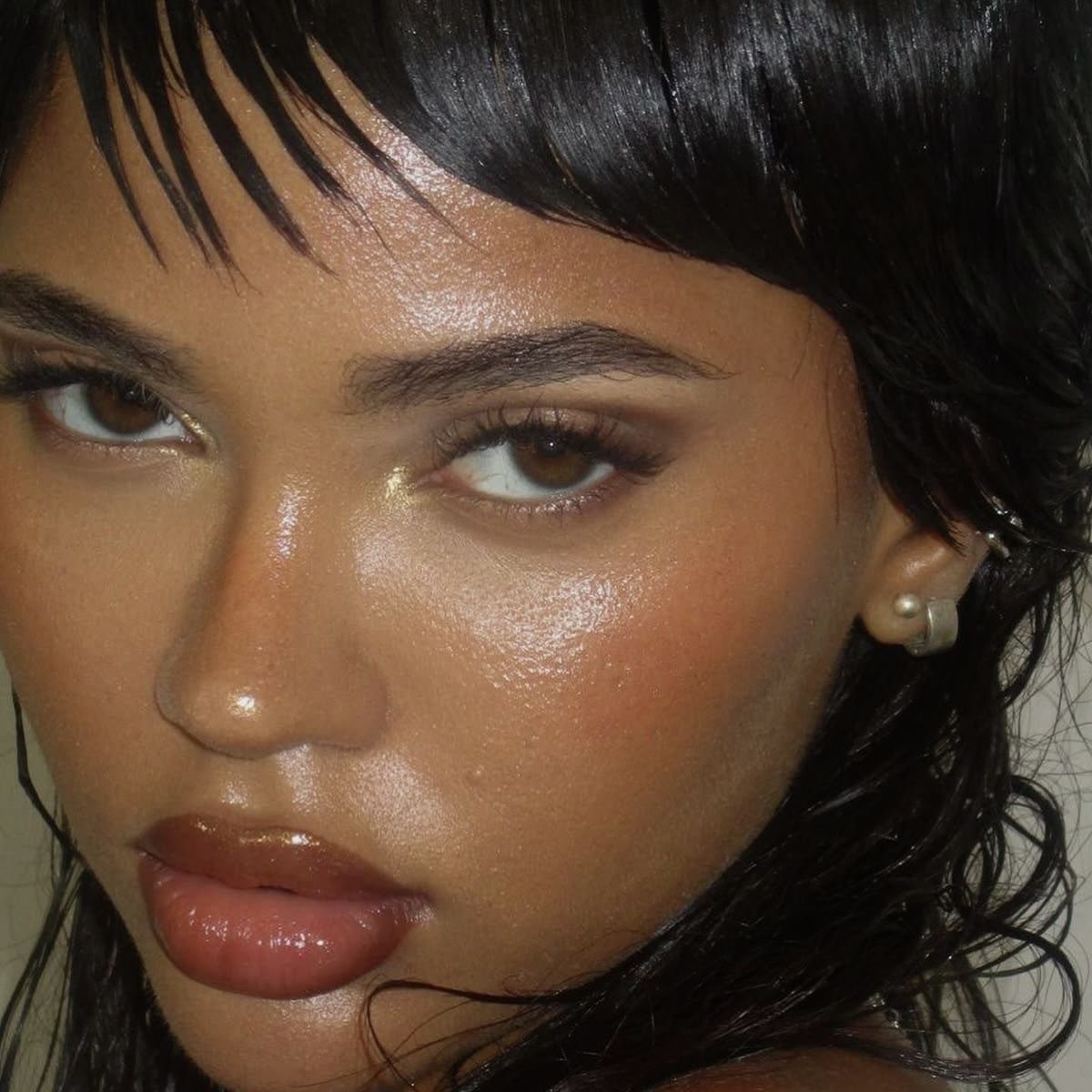 Person with wet hair and glowing, dew-like makeup with glossy brown lips.