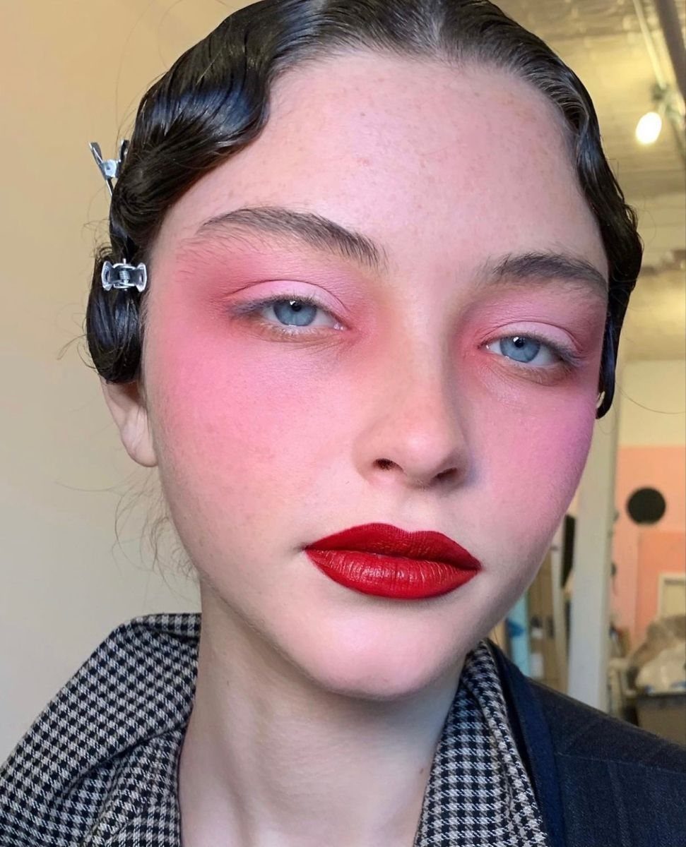 Woman with vibrant pink blush and eyeshadow and bold red lipstick.