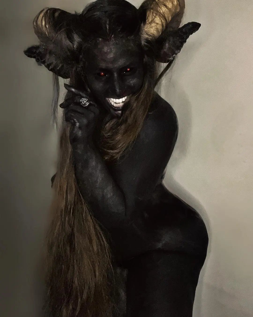 Person with black body paint, glowing red eyes, and large physical horns posing.