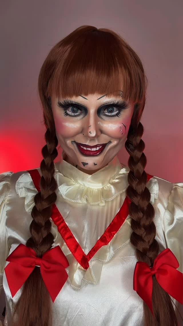 Person with creepy doll face paint, braided pigtails, and white ruffled dress.