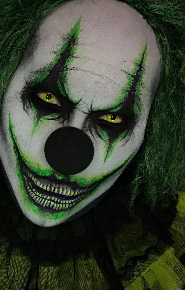 Person with scary clown face paint, yellow eyes, and a wide toothy grin.