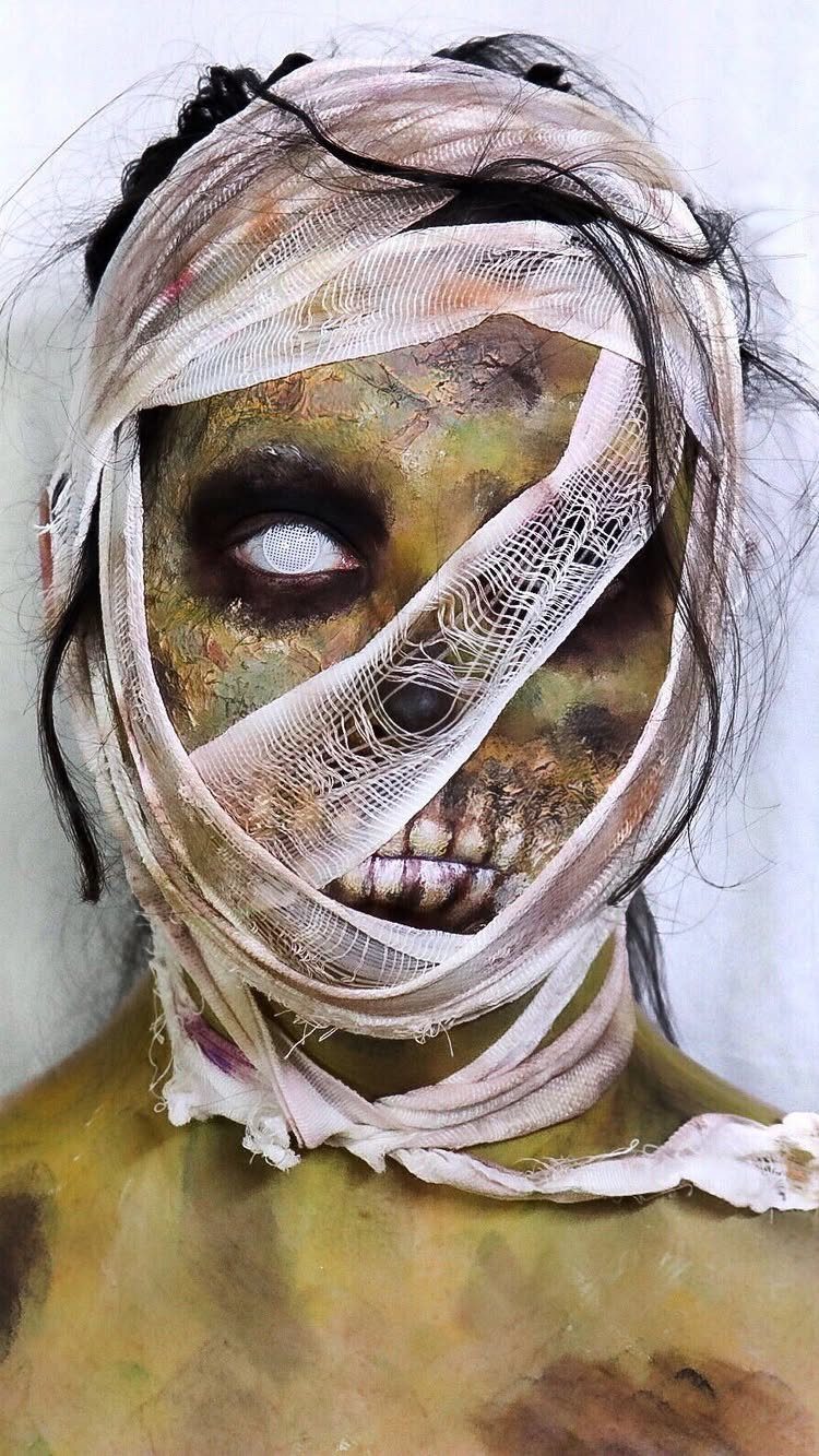 Person with decayed green skin and white gauze bandages wrapped around their head.