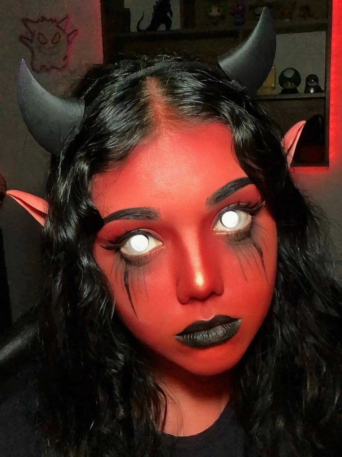 Person with red face paint, black lipstick, and black devil horn headband.