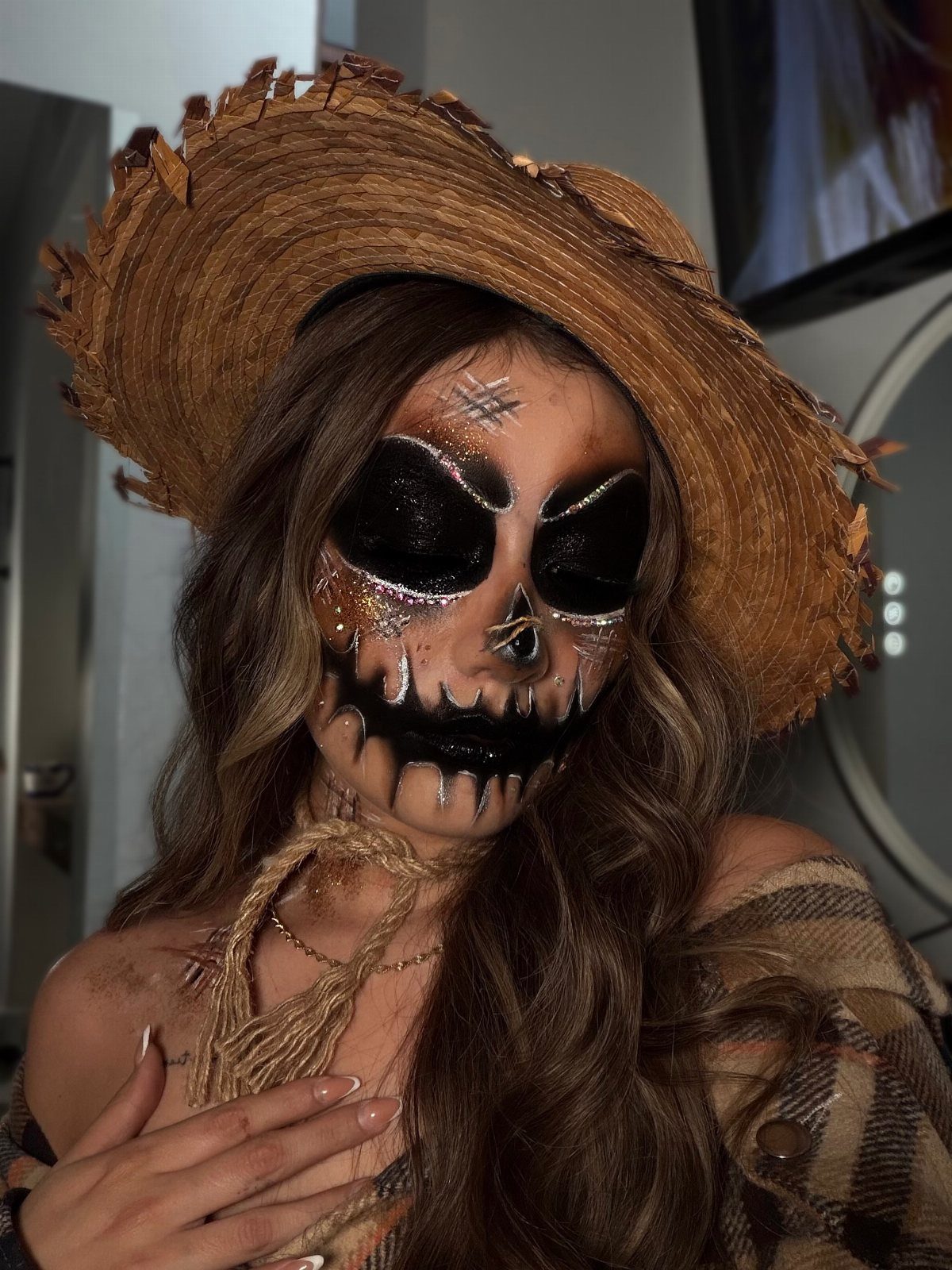 Woman with scarecrow face paint wearing a straw hat and plaid shirt.