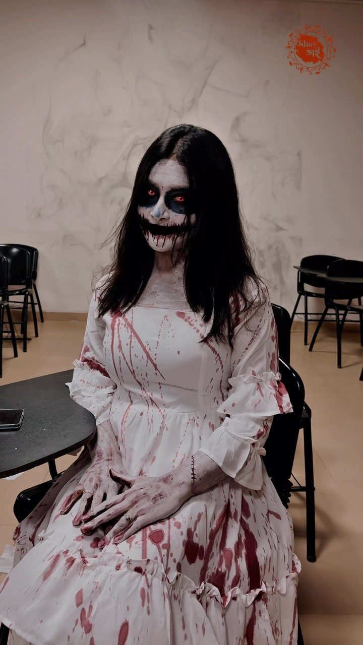 Person in blood-stained white dress with white face paint and wide black smile