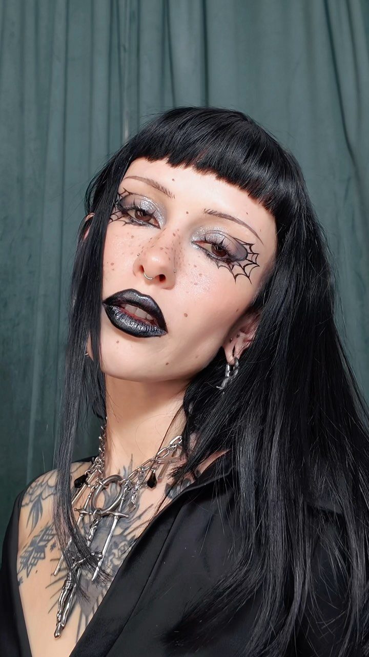 Woman with black hair and spider web face paint around her eyes.