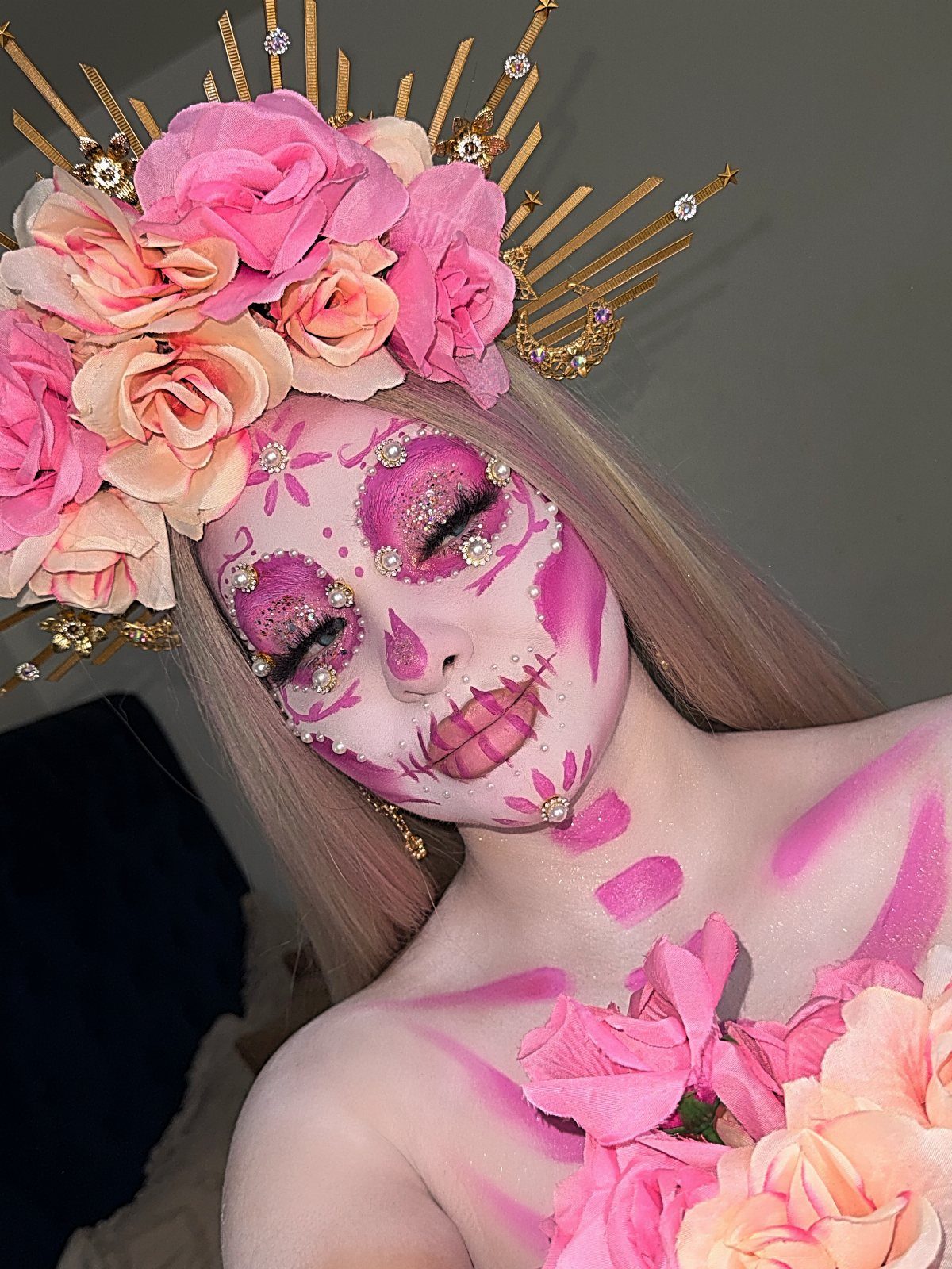 Person with pink and white sugar skull face paint wearing a rose crown.