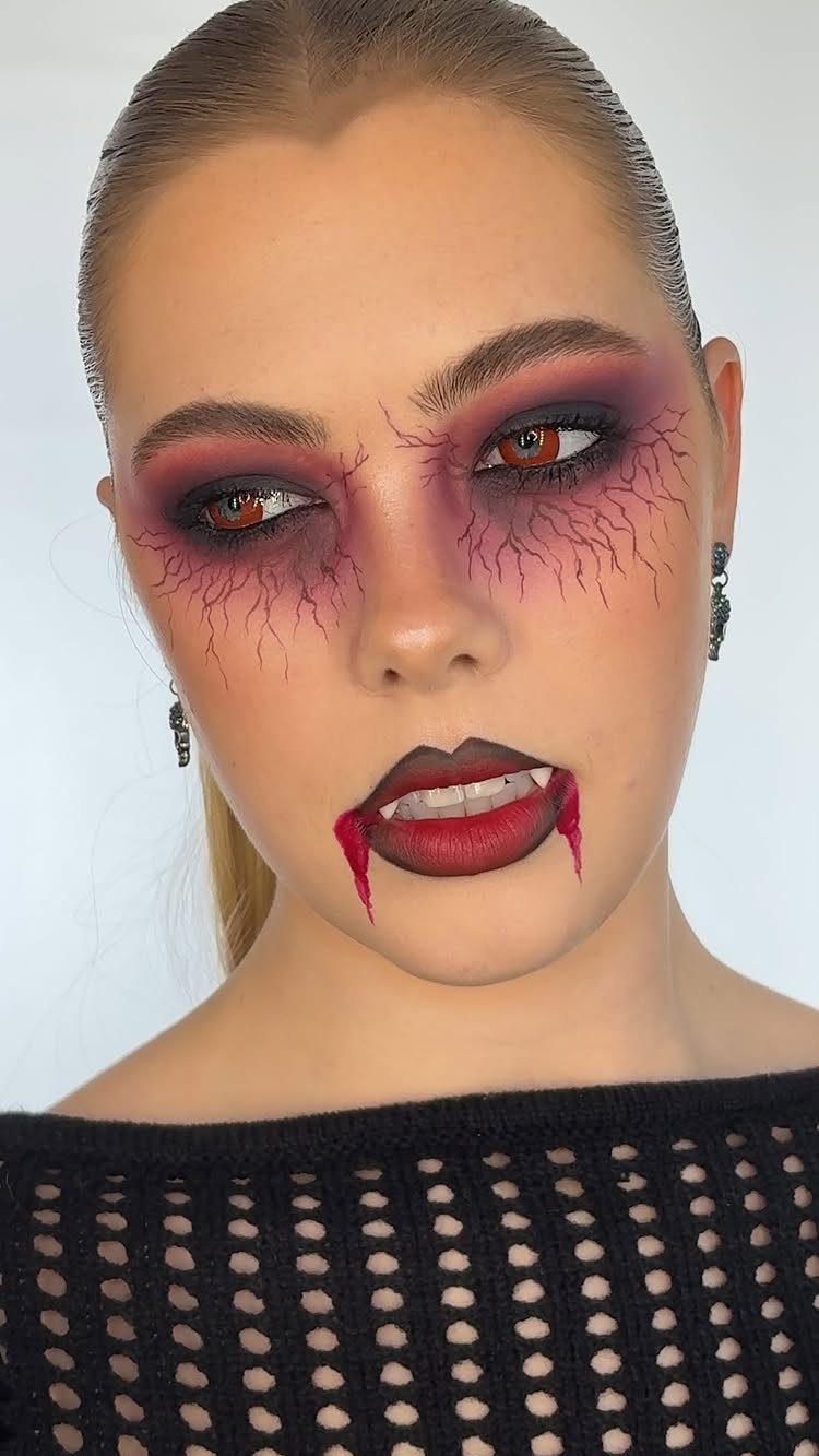 Woman with vampire face paint, prosthetic fangs, and fake blood dripping from lips.
