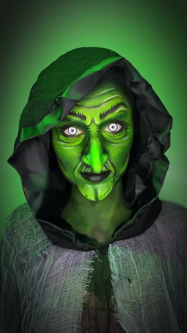Person with green witch face paint, long nose, and a green hooded cloak.