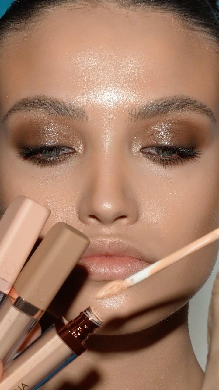 Woman with shimmering bronze eyeshadow and glowing skin posing with concealer products