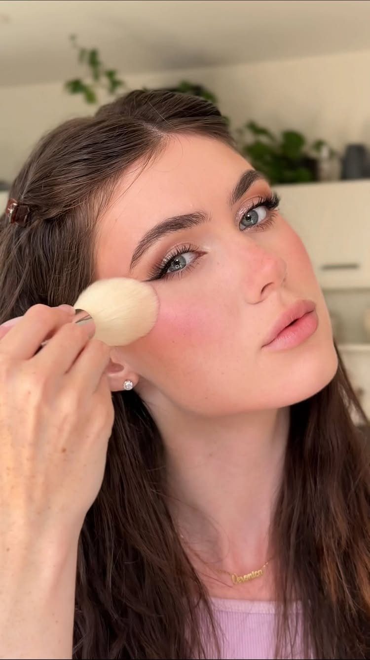 Woman receiving pink blush application on her cheek with a makeup brush
