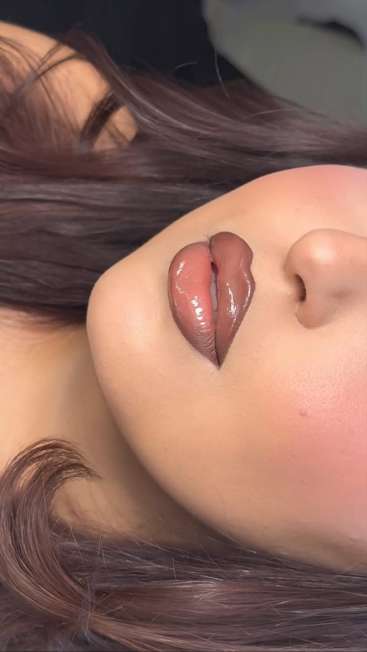 Glossy brown lips and smooth skin on a person with dark brown hair.