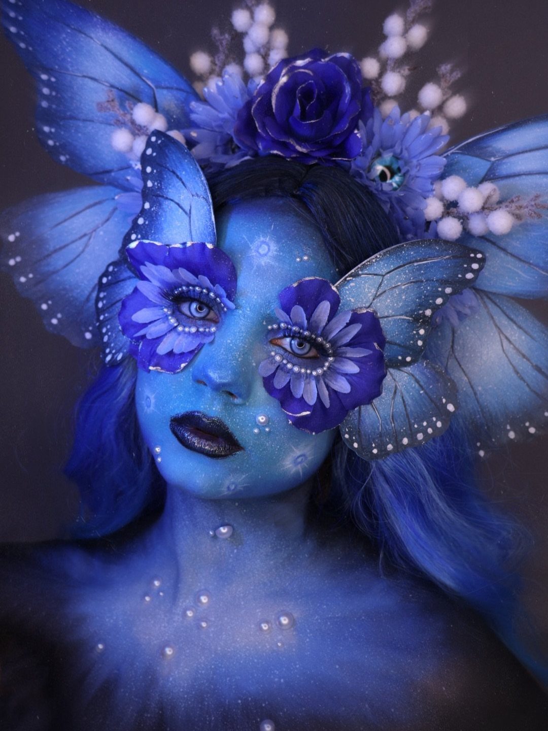 Person with blue skin and butterfly wings wearing a floral crown and makeup.