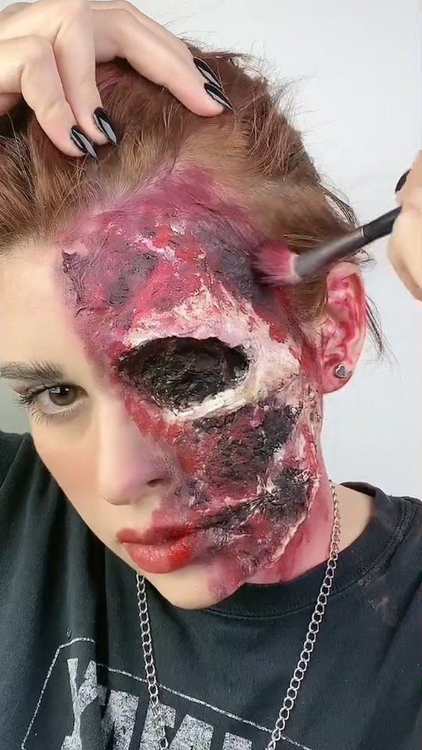 Person with split-face gore makeup showing a decayed, wounded right side of face.