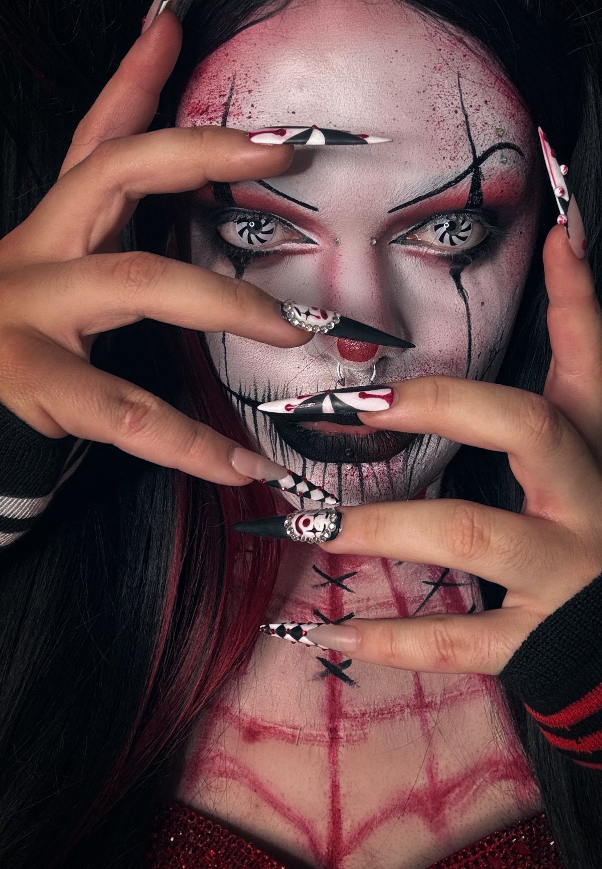 Person with white clown face paint and red stitched details on their chest.