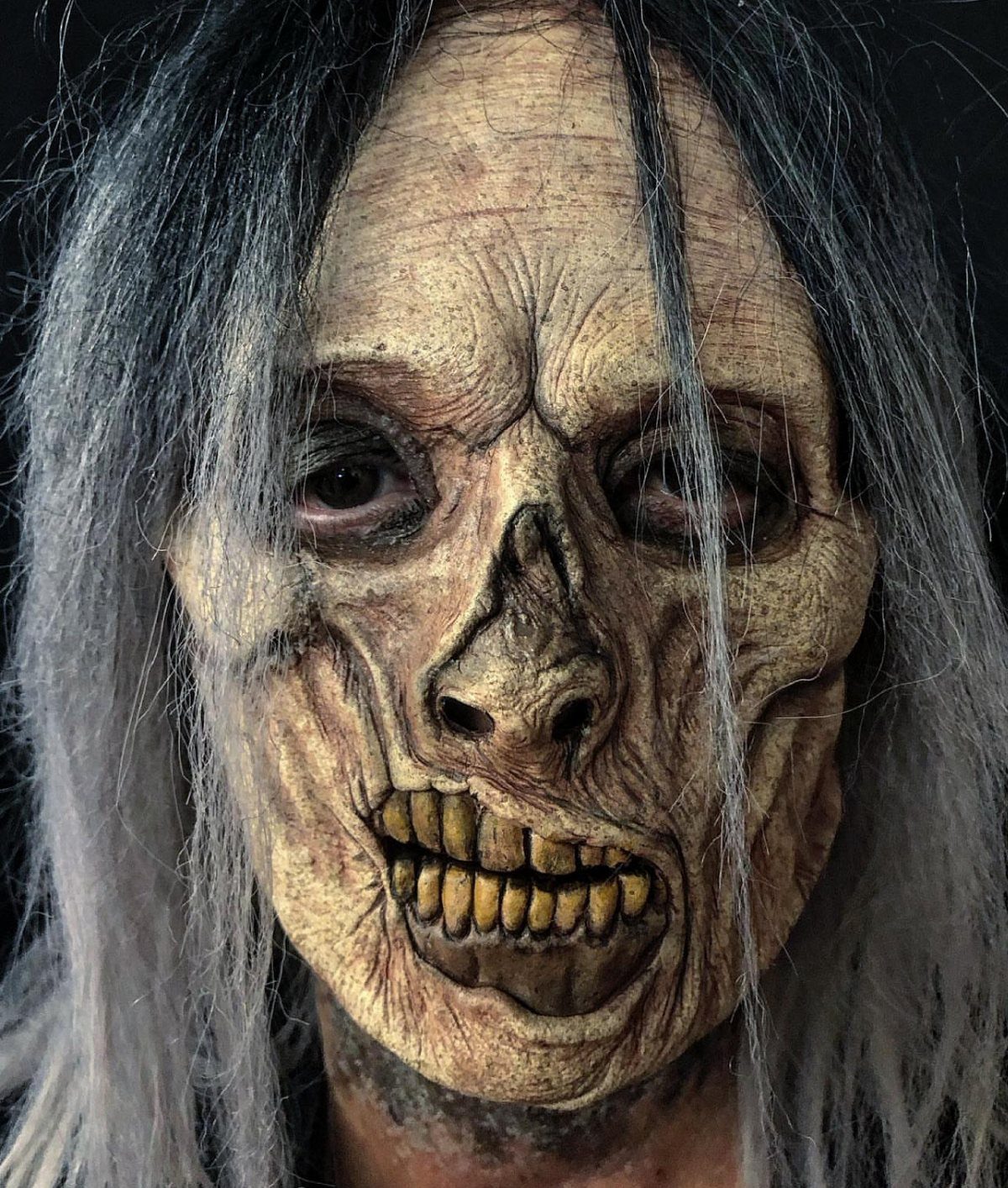 Zombie mask with pale wrinkled skin, skeletal nose, and yellowed teeth with grey hair.