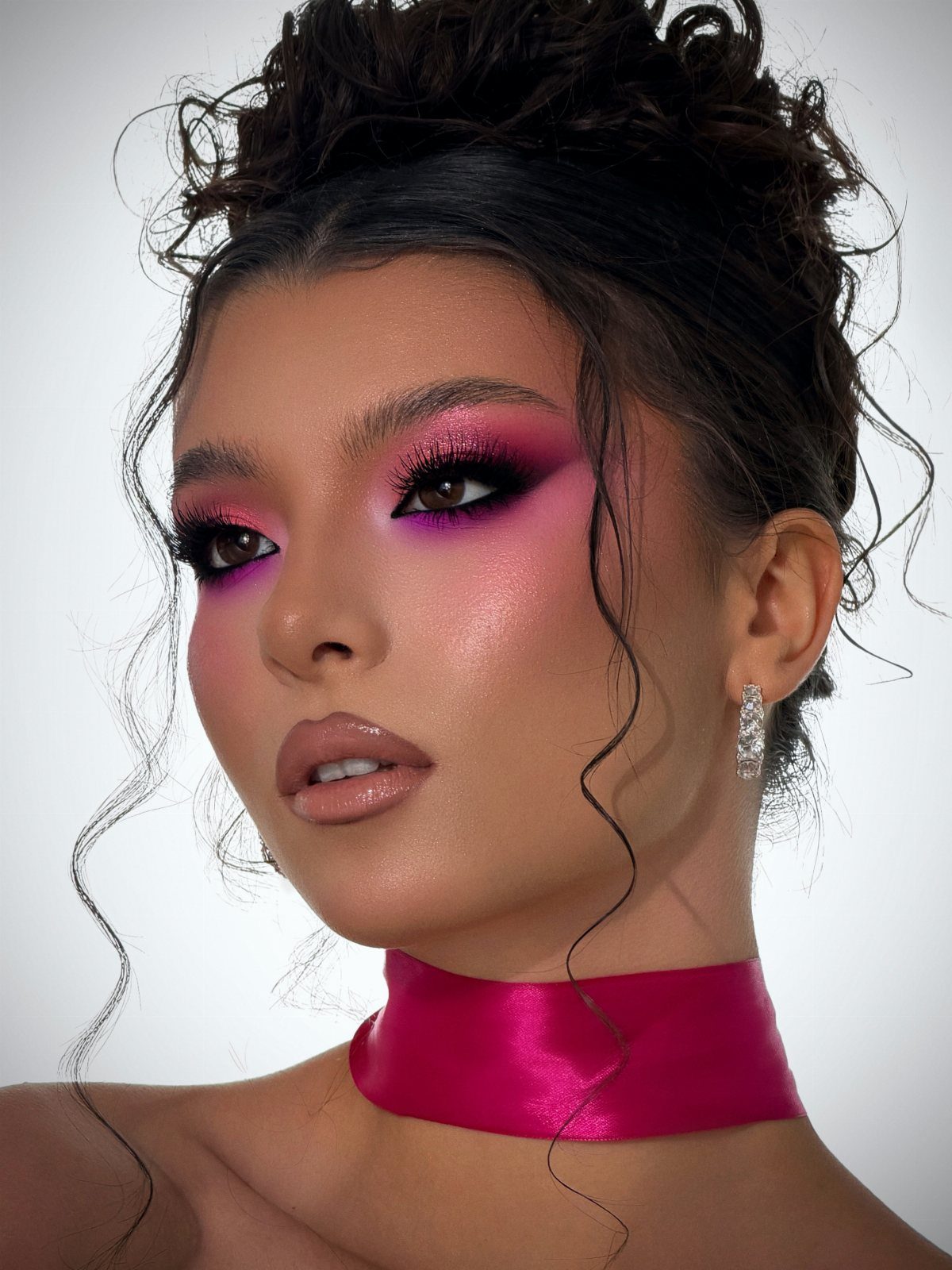 Woman with bold pink and purple eyeshadow, glossy lips, and a pink satin choker.