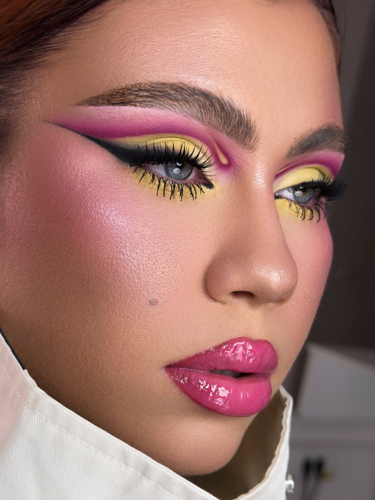 Woman with bold pink and yellow eyeshadow and glossy pink lips.
