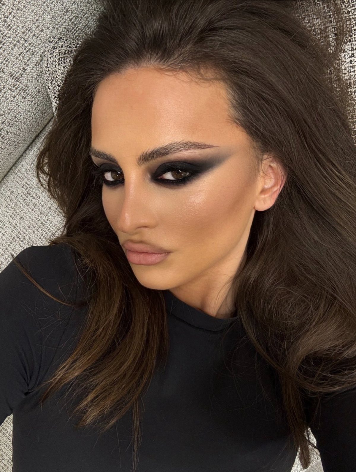 Woman with dramatic dark smoky eye makeup and long brown hair posing.