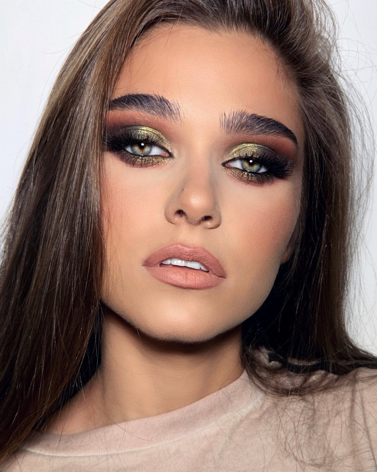 Woman with bold gold and brown eyeshadow and matte nude lipstick posing.
