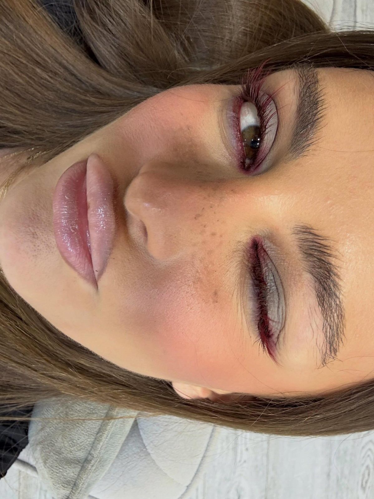 Woman with glossy pink lips and reddish-brown eyeshadow in a close-up portrait.