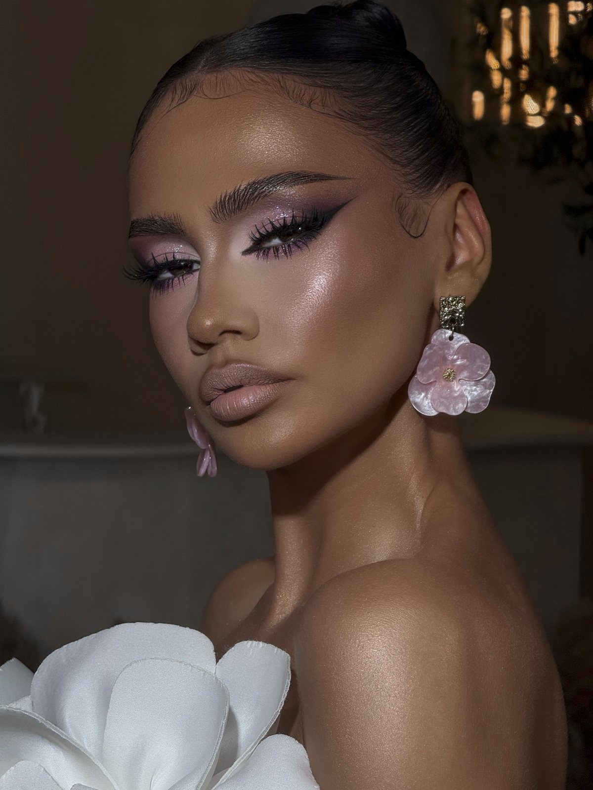 Woman with dramatic purple winged eyeshadow and shimmering highlighter posing for a portrait.