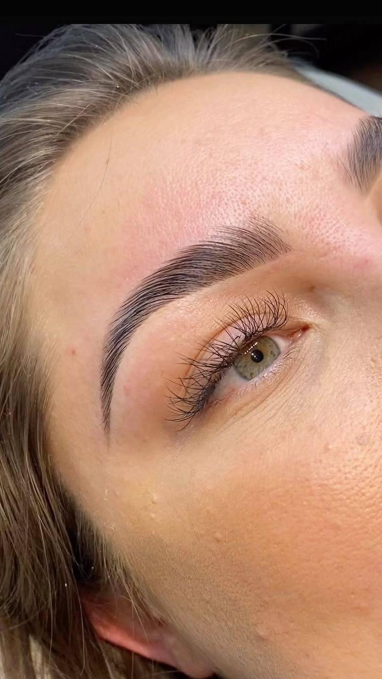 Close-up of a groomed and tinted dark brown eyebrow above a green eye.