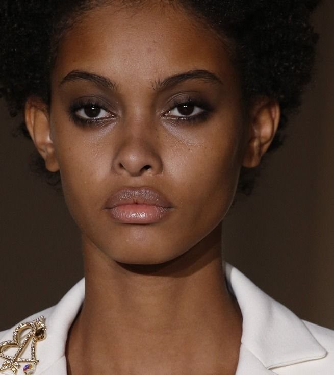 Woman with smudged dark eyeshadow and neutral lips wearing a white blazer.