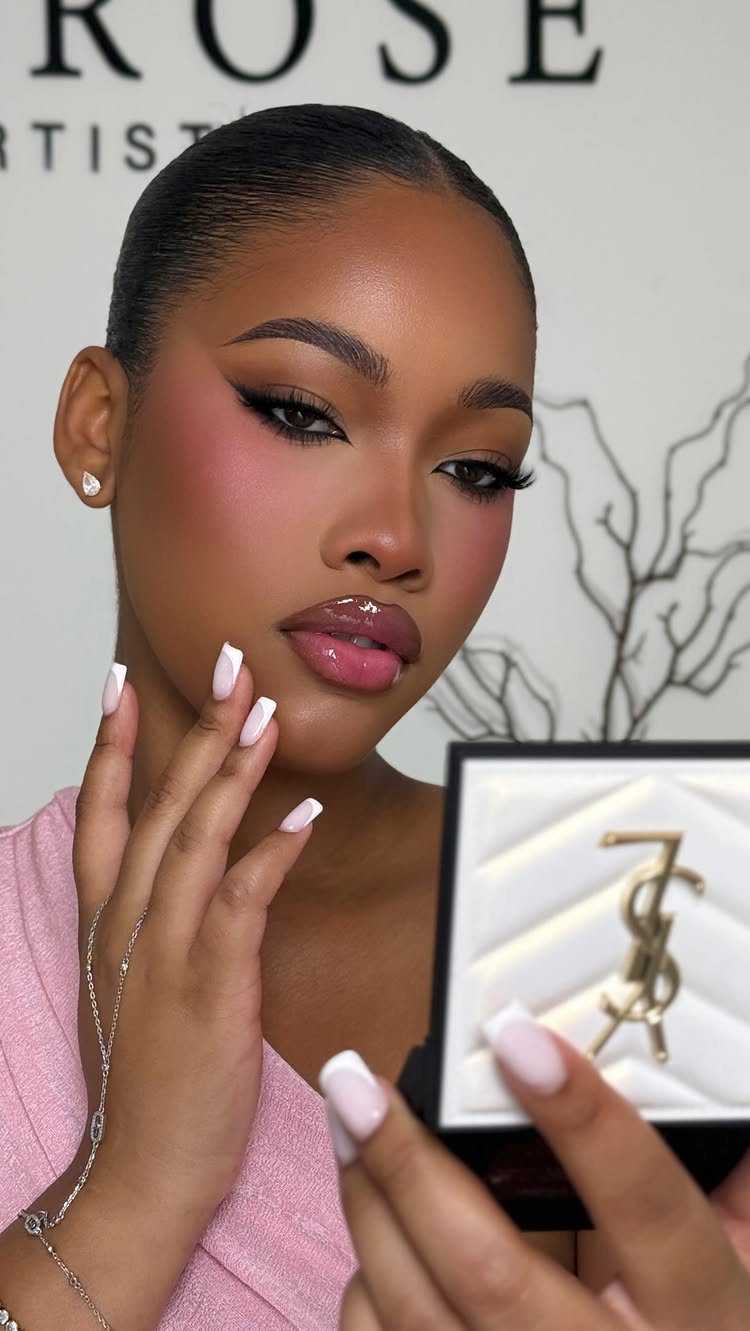 Woman with bold pink makeup holding a gold and white makeup compact.