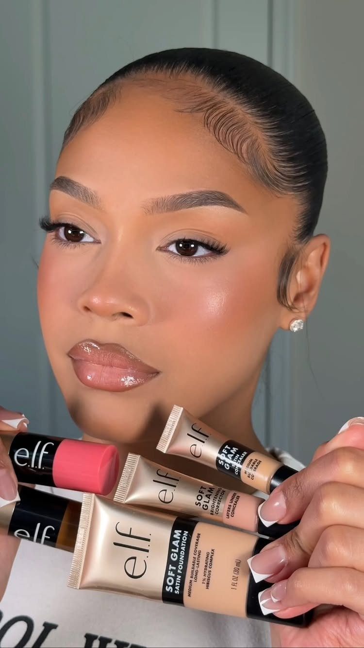 Woman with full makeup holding e.l.f. cosmetics foundation and blush tubes.