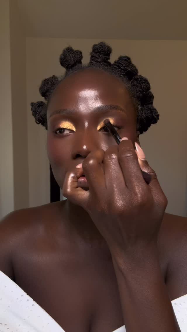 Woman applying gold eyeshadow to her eyelid with a small makeup brush
