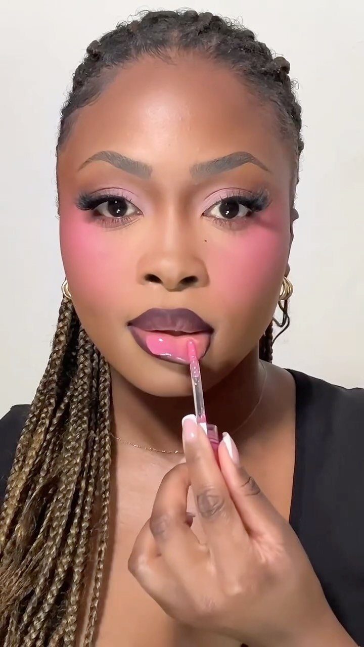 Woman with bold pink makeup applying pink lip gloss to her lips.