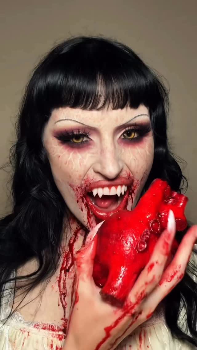 Vampire Eye Makeup Ideas: 8 Looks for Halloween Night 2 Woman with scary vampire makeup and fangs holding a bloody heart prop.