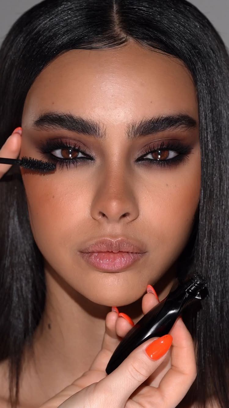 Warm Asian Makeup: 6 Peach, Coral and Red Ideas 6 Woman with warm brown makeup and orange nails applying black mascara to lashes