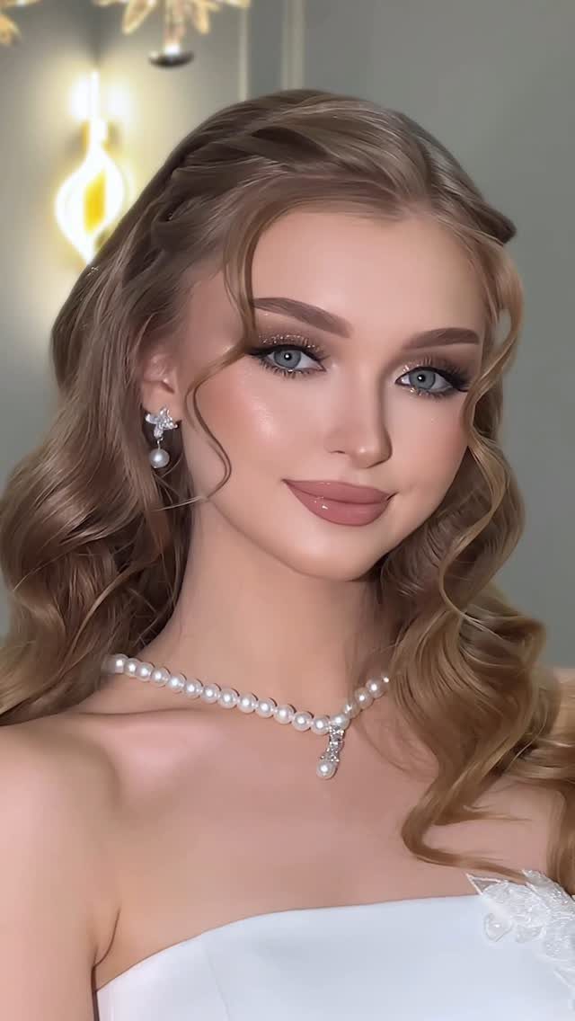 Woman with blue eyes wearing classic bridal makeup, white dress, and pearl necklace.
