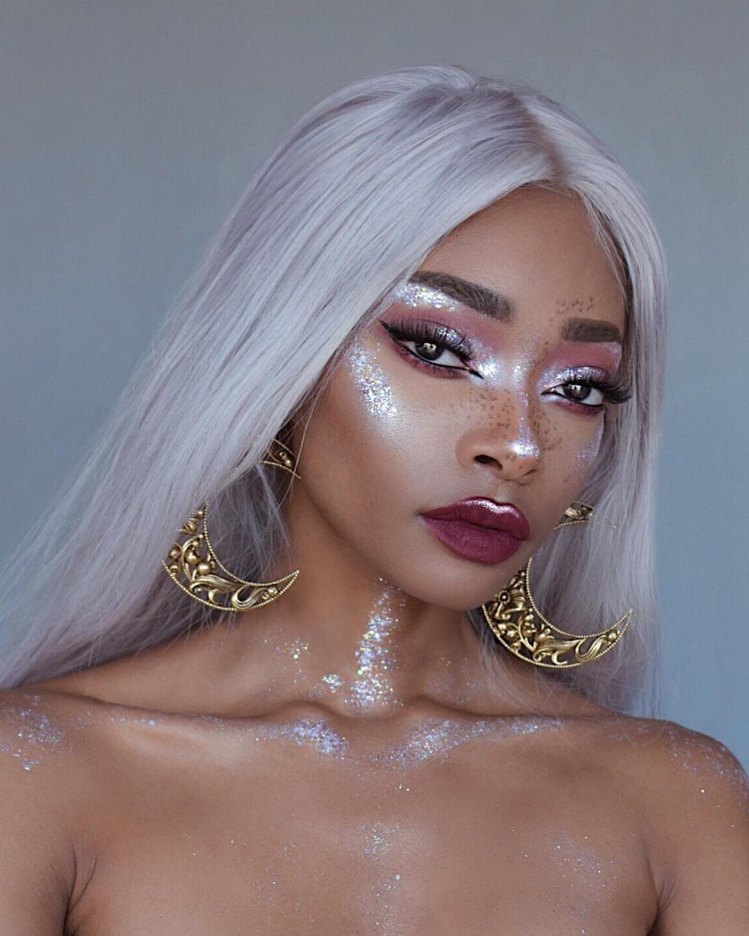 Woman with silver hair and gold moon earrings wearing sparkling body glitter.