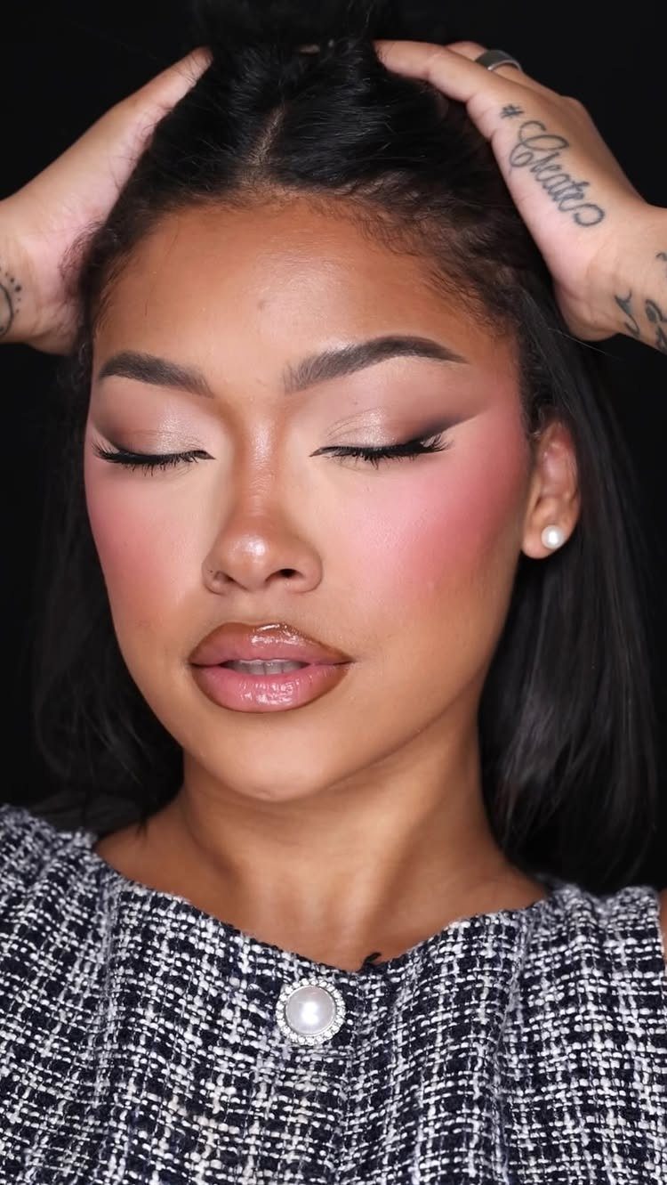 Woman with bright pink blush, glossy lips, and winged eyeliner posing against black.