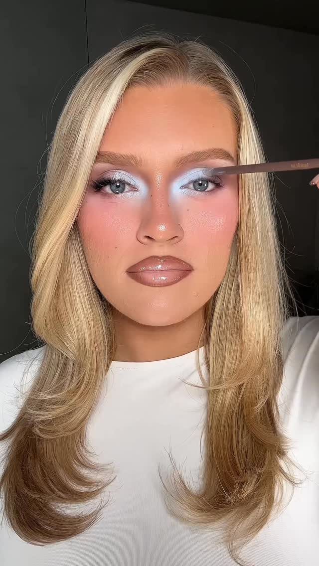 Woman with blonde hair wearing light blue frosted eyeshadow and glossy nude lips.