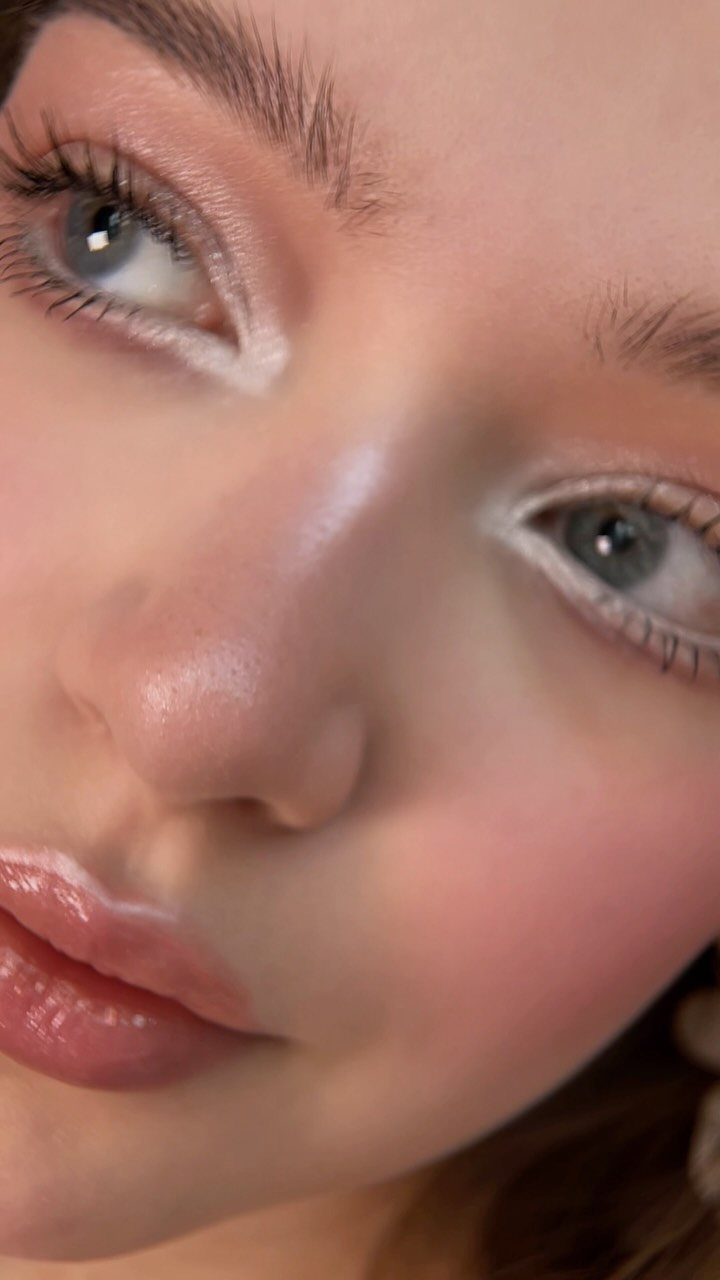Person with shimmering white inner corner highlight, glossy lips, and pink blush.