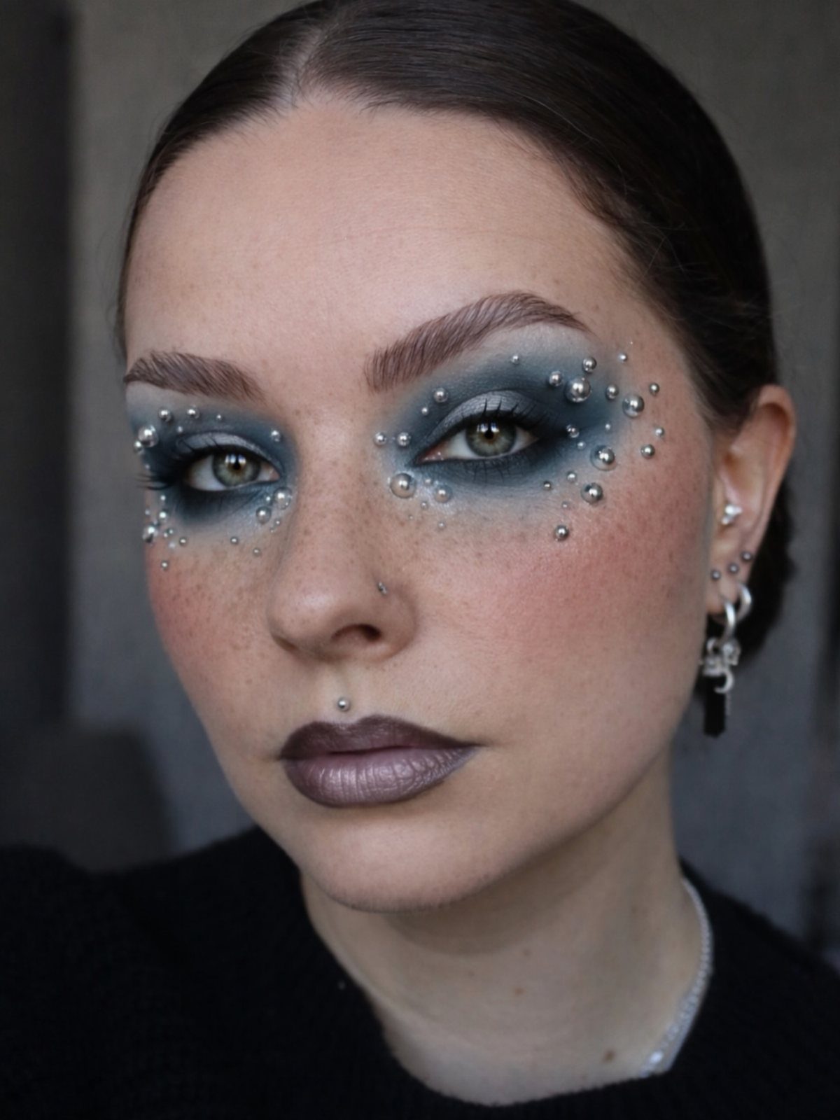 Woman with blue eyeshadow and sparkling rhinestones applied around her eyes and cheeks.